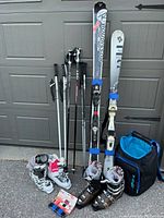 Full display of skis, poles, boots and bag arranged against garage door