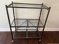 Front view of metal utility rack showing three wire shelves and caster wheels.