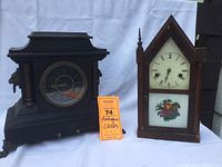Two antique mantle clocks side by side showing overall condition and style: left a black Ingraham Princess with lion details, right a wooden New Haven Clock Company clock with fruit art on glass door.