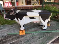 Side view of the wooden cow stool showing black and white painted body, four legs, and overall shape.