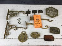 Overview photo showing all brass items in the collection on a white surface including plant hangers, buckles, trivet, and hinges.