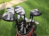 View of Black Steel woods #1, #3, #5 showing club heads positioned in golf bag, outdoors on grass.