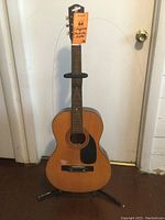 Full front view of the Conqueror acoustic guitar on its stand, showing body, neck, and headstock