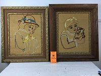 Both framed needlework pictures on burlap, showing one with girl and chicks in gold edge frame (23x27 inches) and one with girl and cat in oak frame (24x28 inches)