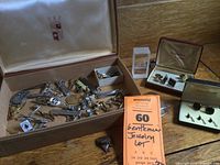 Wide shot showing entire box filled with assorted men's jewelry accessories including cuff links, tie clips, pins, and small trinkets.