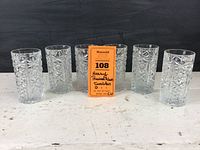 Six heavy pressed glass tumblers photographed in a line to show quantity and style, placed on a white surface with a dark background.