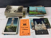 Two large stacks of postcards, left stack labeled New England, right stack US and world. Various black and white and color postcards visible on top.
