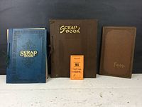Two scrapbooks and one photo album standing upright showing covers with titles 'Scrap Book' and 'Fotofil'