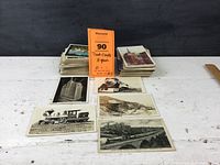 Photo showing a group of postcards stacked and spread out on a table, featuring trains and buildings.