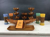 Front view showing all items in the collection including monkey pod dessert cups, woven basket, serving tray, and four colorful ceramic glasses.