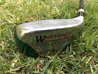 Close-up of the silver metallic club head printed with 'Warrior Custom Golf Tour' showing some wear marks.