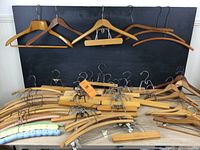 Wide view of the collection of vintage wooden hangers hanging on a wall, showing their various shapes and designs.