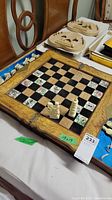 Diagonal view of chessboard showing carved frame and painted floral squares. Chess pieces partially placed on board.