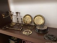 Shelf with brass candelabra, miniature candlesticks, brass key-shaped key holder, horse brasses, silver plate coasters with stand, and other brass items.