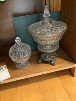 Photo showing both covered crystal candy dishes with detailed cut patterns including the larger dish on a metal base and smaller with pedestal base.