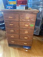 Wooden game chest with nine drawers and wooden handles, sitting on wooden floor.