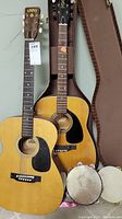 Two acoustic guitars, one Capri branded, with two tambourines placed in front and a brown soft guitar case behind.