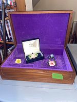Wooden jewelry box with purple velvet interior, containing four floral brooches including Royal Doulton boxed rose brooch, Benton England blue flower brooch, and two other floral brooches.