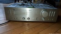 Front left angle view of JVC AX-1 stereo integrated amplifier receiver showing the silver metal faceplate, tuning dial, audio control knobs and switches, and power cord.