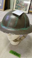 Metal army helmet with green patina shown from front angle on mannequin head