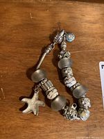 Full view of the bracelet laid flat showing starfish charm, glass and metal beads in white and silver tones, and clasp with Pandora branding.
