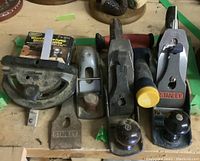 Four Stanley hand planers with wooden and metal knobs, a wheel and circle cutter in original packaging, and a Stanley metal measuring tool with yellow knob on a wooden surface.