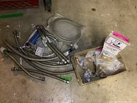 Overview of plumbing connectors and accessories laid out on basement floor including flexible braided steel supply lines, coiled hoses, and packaged accessories.