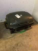 Closed portable propane BBQ grill with black body, two handles, and temperature gauge on lid