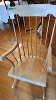 Front angle of the wooden rocking chair showing the seat, armrests, and spindled curved backrest.