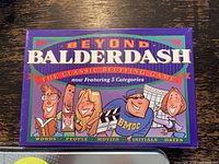 Photo of Beyond Balderdash classic bluffing game box in purple color with five category icons and cartoon characters on the cover.