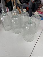 Six clear crackle glass sconces arranged on table showing varying height and glass texture.