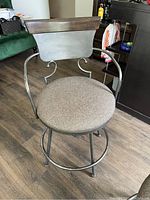 Front-side view of a metal framed bar height swivel chair with a gray upholstered round seat, curved armrests, and a wood and metal backrest.