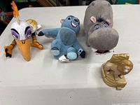 Photo showing three plush toys from Lion King: Zazu, young Simba, and a happy hippo, plus a small plastic lion figure on a base.