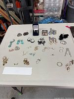 Overview of all 29 pairs of pierced earrings laid out on a white table, showing variety in style and color.