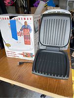 George Foreman grill with box, open to show ribbed grilling surfaces on both bottom and top plates.