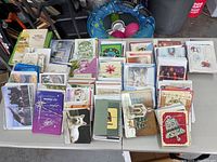 Photo showing a large assortment of mostly holiday and greeting cards arranged on a table. Cards sorted in stacks by style with visible Christmas and seasonal themes.