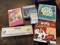Photo showing multiple kids games and an 80-piece jigsaw puzzle with colorful boxes and logos including Yahtzee Princess Edition, Snug Bug Rug, Bingo cards, Gib Gab, and Wipe Catapults.