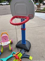 Photo of Little Tikes adjustable basketball hoop with red rim and black base, pink push walker, ball popper toy, and toy race track
