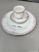 Set of Mikasa Emily pattern dinnerware including dinner plate, saucer, and cup showing the floral pink border design and gold rim on cup