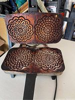 Open electric pizzelle maker showing the two patterned baking plates with intricate floral designs molded for pizzelle cookie baking.