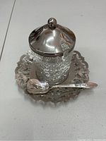 Photo showing crystal sugar bowl with silver plated lid and matching silver plated spoon on serving tray.