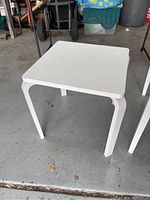 Smaller white square table with rounded corners on concrete floor