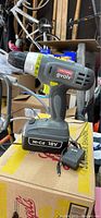 Side view of Craftsman Evolv cordless drill with attached 18V Ni-Cd battery and charger sitting on a box.