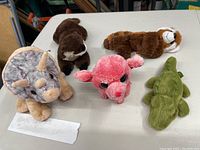 Five Wild Republic stuffed animals: a gray triceratops dinosaur, brown beaver, brown otter, pink pig, and green alligator arranged on a table.