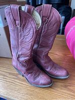 Pair of reddish-brown leather cowboy boots with decorative stitching, visible evidence of repairs, size 5.5