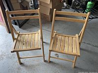 Two wooden folding chairs standing side by side, showing the front and seat design.