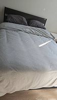 Full view of made queen bed with dark wooden frame and grey bedding including pillows, sheets, and comforter.