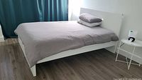 Full view of assembled white IKEA bed with mattress, pillow, and cinnamon-colored duvet cover, showing modern clean lines and low footboard.