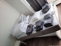 Photo of assembled IKEA white bed with mattress and bedding including pillows and folded blankets on top.