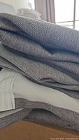 Folded gray woven fabric drapes showing the texture and layering, lying on a surface.
